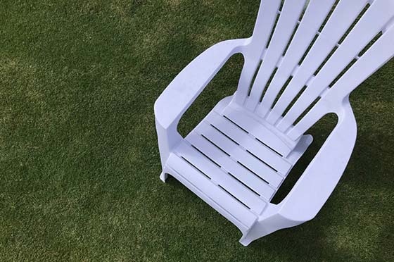 Photo of a white chair sitting on lush green lawn | Featured image for DIY Turfing Page by Centenary Landscaping Supplies.