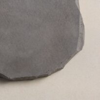 CentenaryLandscapePaversAug202_028 Round, dark grey concrete paver with a textured surface and irregular edges.