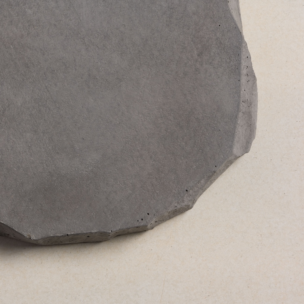 CentenaryLandscapePaversAug202_028 Round, dark grey concrete paver with a textured surface and irregular edges.